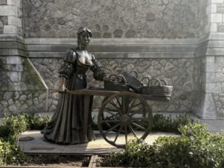 The bronze Molly Malone statue with her cart of cockles against a stone wall in Dublin, Ireland