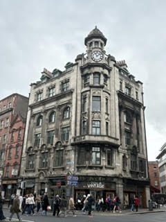 A Victorian building with a domed clock tower above a busy pedestrian street corner in Dublin, Ireland