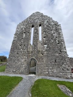 The roofless stone gable of a ruined medieval abbey with tall narrow windows on green grass in Ireland