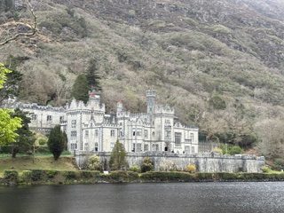 Kylemore Abbey's white stone facade beside the lake beneath a wooded hillside in Connemara, Ireland
