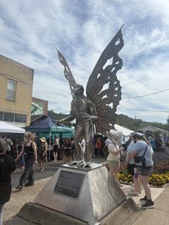 The metal Mothman statue with outstretched wings amid a festival crowd in Point Pleasant, West Virginia