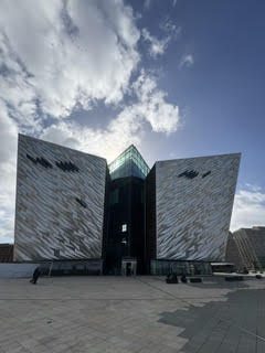 The angular, shimmering facade of the Titanic Belfast museum under a bright cloudy sky in Northern Ireland